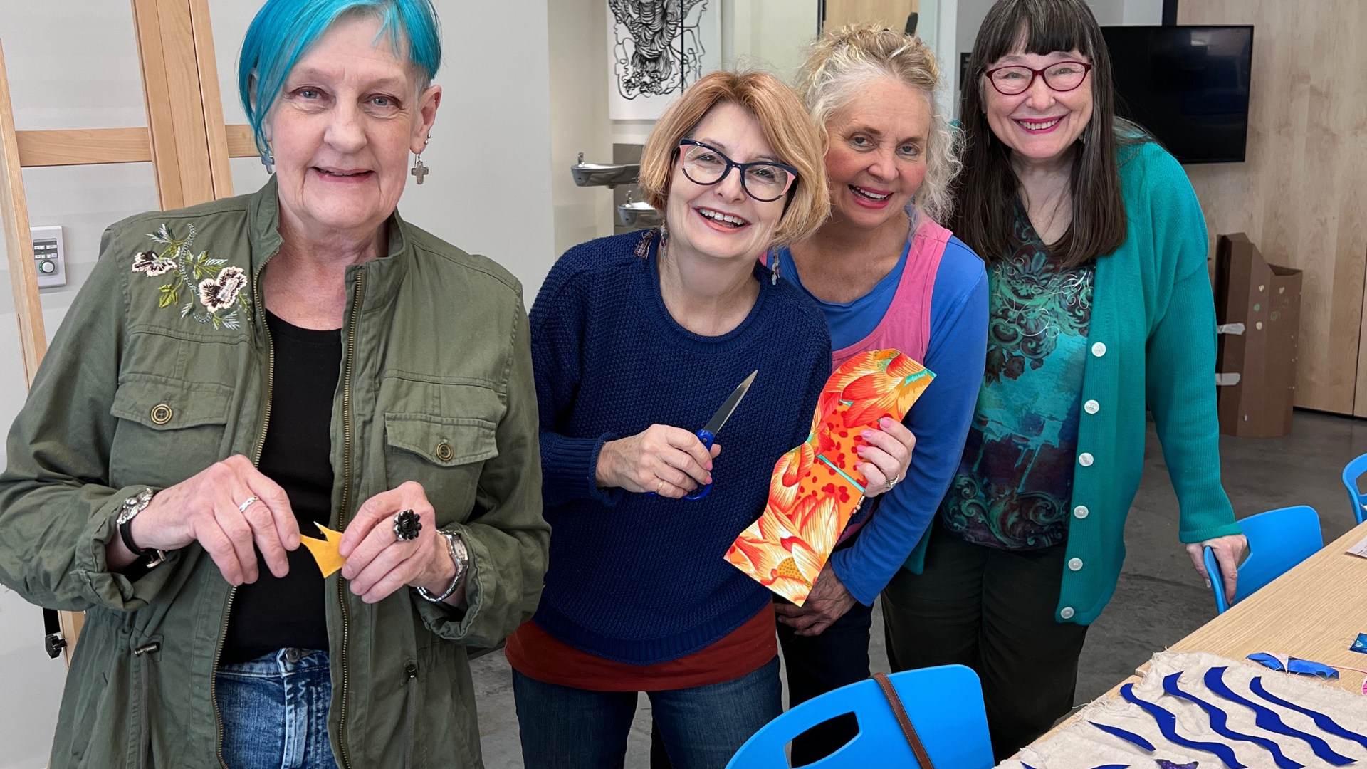 Four women standing by a table with crafts on it and smiling.
